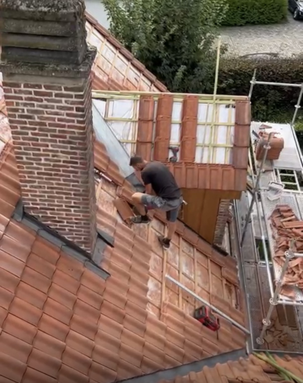 Man in werkplaats met ruitjeshemd en schort, leunend op houten planken, achtergrond met stapels hout.